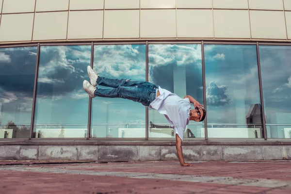 athlete guy dancer in white T-shirt, jeans, jump his arm, summer city, sunglasses, background glass windows, active hip hop youth lifestyle acrobatic stunt break dance, street and fashionable artist,
