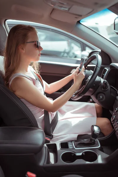 A woman driving car, sitting in mobile phone, writing message in parking lot near shopping center, waiting for friends, online application on Internet, long waiting for her husband at store. — Stock Fotó