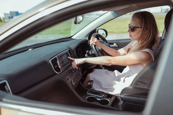 Woman driving a car, selects navigation on display screen, turns on voice assistant, selects the application on the screen of the navigation map in the car. Right-hand drive, left-hand drive.