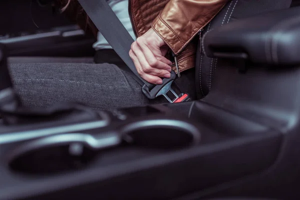 Close-up, uma mão feminina prende um cinto de segurança em um carro, jaqueta de couro de fundo no verão na primavera e no outono, segurança no trânsito no carro . — Fotografia de Stock