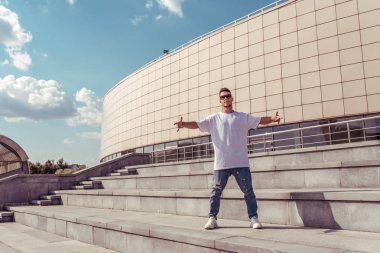 güçlü sportif erkek dansçı, güven poz ayakta, genç adam, moticavia metin için boş alan, arka plan adımları ve bina karşı yaz şehirde, kot güneş gözlüğü, beyaz bir t-shirt