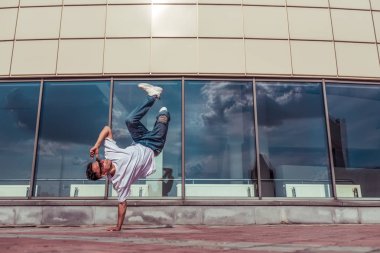 güçlü sportif adam dans break dans, bir kol kırmızı saçlı, genç adam, motivasyon bir metin için boş alan, bina cam pencerelerin yaz şehir arka plan, kot pantolon, güneş gözlüğü, beyaz T-shirt duruyor