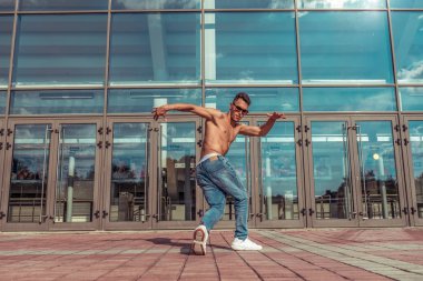 güçlü sportif adam dans break dans, çıplak gövde şişirilmiş, genç adam, boş alan metin yaşam tarzı motivasyon, arka plana karşı yaz şehir bir cam bina penceresi, kot güneş gözlüğü, hareket