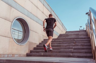 Bir erkek atlet, arkadan bir görünüm, şehirde yaz aylarında, merdivenlerde bir çalışma sabah çalışır. Spor giyim tişört şort. Fitness, gençlik yaşam tarzı, şehirde sağlıklı yaşam tarzı. Metin için boş alan.