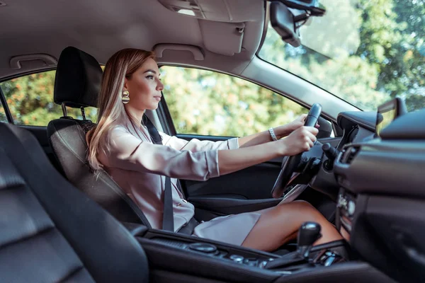 Beautiful girl business lady driving a car, summer in the city, pink-beige formal suit, a trip to work, long hair casual makeup. Box automatic tanned womans skin. — Stock Photo, Image