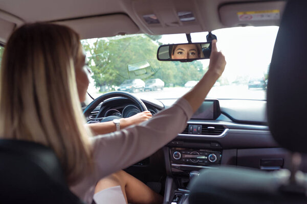 женщина за рулем автомобиля, в летнем городе, зеркало заднего вида, парковка, разворот, оглядывается назад ряд сидений, проверяет детей на заднем диване, контролирует задний ряд сидений с пассажирами
.