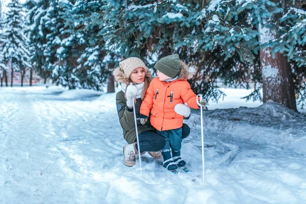 Seorang ibu muda mengajarkan seorang anak laki-laki berusia 3-5 tahun, bermain ski untuk anak-anak, di musim dingin di hutan, berlibur, sebuah resor di taman bersalju, salju latar belakang melayang pohon . — Stok Foto