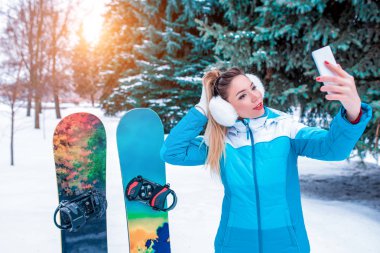 sokakta kışın güzel kız selfie fotoğraf, arka plan kar ağaçları, kar drifts, yeşil ladin. Snowboard kayak tahtaları. Kış kayak merkezinde dinlenebilirsiniz. Cep telefonu görüntülü arama, online sosyal ağlar.