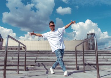 Genç erkek dansçı, şehirde yaz aylarında, dans break dans, sağlıklı fitness atlet yaşam tarzı, beyaz t-shirt, kot spor ayakkabı. Müzikle dans ediyorum. Herkese açık olarak gerçekleştirir.
