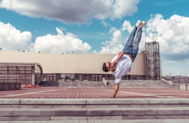 genç şık adam ayakta bir kol, erkek dansçı, yaz şehir, dans break dans, sağlıklı fitness sporcular yaşam tarzı, beyaz t-shirt kot pantolon. Müzikle dans etmek. Halka açık olarak gerçekleştirir. Metin için boş alan.