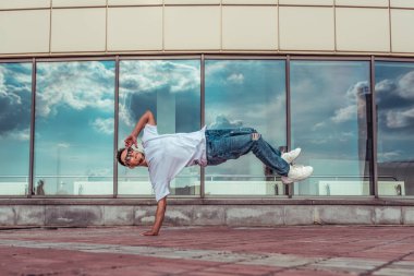 Genç şık adam pencere bulut arka plan, bir yandan uçan hava, adam dansçı, yaz kenti, dans break dans, sağlıklı fitness atlet yaşam tarzı, beyaz T-shirt, kot pantolon. Müzikle dans etmek.