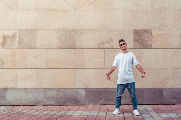 Young stylish man background wall, guy dancer, summer city, dancing break dance, healthy fitness athlete life style, white t-shirt jeans sneakers. Dancing music. Performs public. Free space for text. — Stock Photo, Image