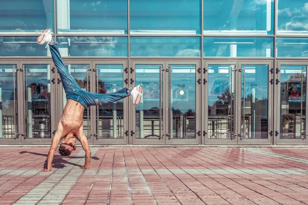 Young guy man stylish athlete background glass windows, standing arms, guy dancer, summer city, dancing break dance, lifestyle healthy fitness. Dancing to music. Performs public. Free space text.