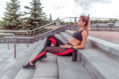 güzel Kadın atlet, oturma adımları, cep telefonu ellerini tutarak, kulaklık ile müzik zevk dinleme, yaz şehir sabah koşmak egzersiz, fitness motivasyon genç kadın yaşam tarzı.