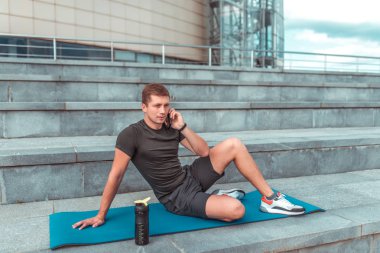 Bir erkek atlet telefonda arama, bir egzersiz sonrası dinlenme, fitness yaşam tarzı tarzı motivasyon patlak verecektir. Şehirde yazın. Su ve protein ile Shaker, bir akıllı telefon üzerinde konuşurken.