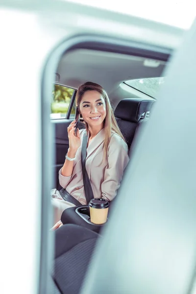 Kaunis liiketoiminnan nainen auton sisustus, matkustajajuna taksi, älypuhelin käsissä, onnellinen hymyilevä nainen tervehtii matkustaja ystävä tyttöystävä, avoin auton ovi, kuppi teetä kahvia, kiinnitetty turvavyö . — kuvapankkivalokuva