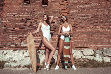 İki kız kız tuğla duvar, yaz şehir, güneş gözlüğü mayo, kaykay, longboard, gençlik yaşam tarzı, sağlıklı hipster moda güneşleniyor. Modern tarzda kadınlar. Boş alan metni.