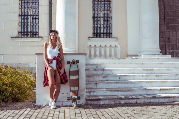 Schöne Frau im Sommer in der Stadt wartet auf Freunde und Freundinnen. Skateboard, Entspannung nach sportlicher Fitness, Workout. braun gebrannte Figur mit langen Haaren. Freiraum für Text. — Stockfoto