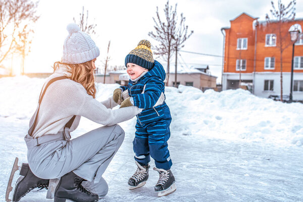 Mom with baby boy 3-5 years old, learn to train, ride in winter city on rink, ice skating. Happy smiling children play having fun weekend weekend first steps child ice skating. Free space for text.