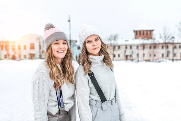 Zwei Mädchen Winterfreunde warme Kleidung, Pullover Hüte, glücklich lächelnd, Entspannung am Wochenende Wintersportort, Schlittschuhlaufen, Hintergrund Schneeverwehungen, Wintereisbahn. fröhliche Frauen. Freiraum für Text. — Stockfoto