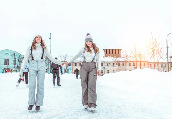 Two women girlfriends winter warm clothes, sweaters hats, happy smiling, relaxing weekends winter resort, ice skating, snowdrifts background, winter ice rink. Cheerful women. Free space for text. — Stock Photo, Image