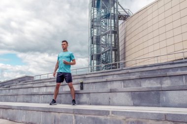 Yaz kentinde erkek sporcu, kulaklık, cep telefonu, zamanlayıcı, zaman eğitimi, temiz hava ile müzik dinler. Gençlik yaşam tarzı, aktif modern erkek atlet, metin motivasyonu için boş alan.
