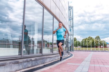 Bir erkek sporcu atlama eğitiminde, hızlı ve güçlü bir hızla, yazın şehirde, öğleden sonra temiz havada koşar. Gençlik yaşam tarzı, aktif modern erkek atlet, metin motivasyonu için boş alan.