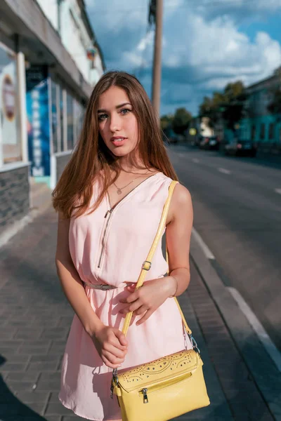 Módní a stylová žena, krásná dívka v růžových šatech v létě ve městě, v rukou žluté kabelky, šťastný pózování čeká na přátele a přítelkyně. — Stock fotografie