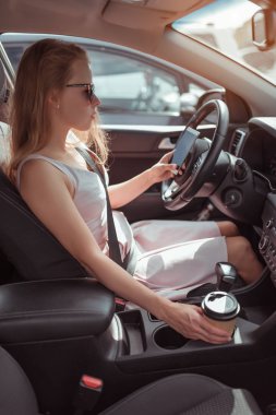 Kadın arabasının içinde kahve fincanı var, alışveriş merkezinin yakınında cep telefonu otoparkı mesajı yazıyor. Uzun bir bekleme yolu trafik sıkışıklığı, park yeri yaz şehri, pembe elbise. otomatik vites kutusu.