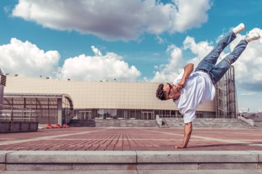 genç adam beyaz bir t-shirt bir dansçı, kot pantolon, şehirde yaz aylarında dans break dans, güneş gözlüğü, beyaz spor ayakkabı arka plan bina bulutlar, aktif hip hop, gençlik yaşam tarzı