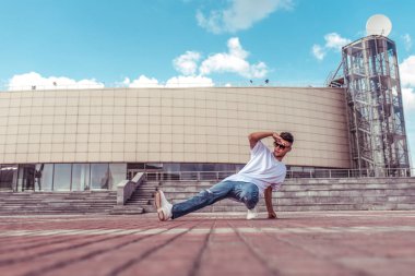 genç adam beyaz bir t-shirt bir dansçı, kot pantolon, şehirde yaz aylarında dans break dans, güneş gözlüğü, beyaz spor ayakkabı arka plan bina bulutlar, aktif hip hop, gençlik yaşam tarzı