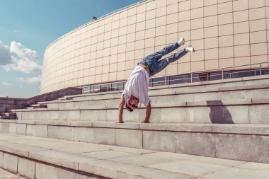 genç adam beyaz bir t-shirt bir dansçı, kot pantolon, şehirde yaz aylarında dans break dans, güneş gözlüğü, beyaz spor ayakkabı arka plan bina bulutlar, aktif hip hop, gençlik yaşam tarzı