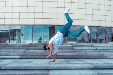 genç adam beyaz bir t-shirt bir dansçı, kot pantolon, şehirde yaz aylarında dans break dans, güneş gözlüğü, beyaz spor ayakkabı arka plan bina bulutlar, aktif hip hop, gençlik yaşam tarzı