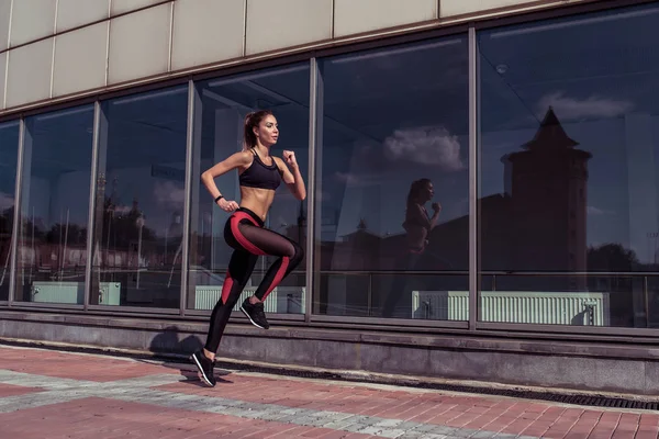 Linda atleta bronzeada atleta menina correr verão cidade vidro de fundo janelas, espaço livre para fitness motivação texto. Roupa de desporto. Caneleiras. Topo. Sapatilhas. Elegante mulher elegante esbelta . — Fotografia de Stock