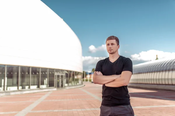 Manlig idrottsman, sommar i stad, står modigt tittar på avstånd, utbildning i frisk luft, är tränare vilar, träning gratis utrymme för text motivation fitness träning. Svart T-shirt shorts. — Stockfoto