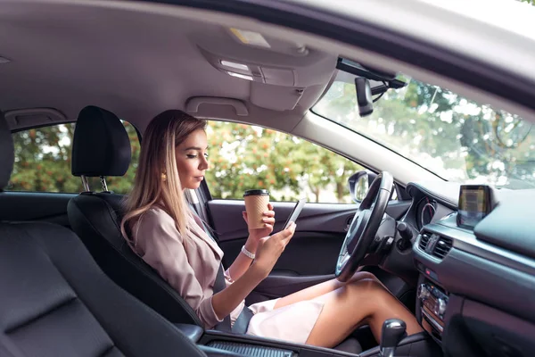 Mujer conducir coche ciudad de verano, estacionamiento atasco de tráfico mientras espera, mira el teléfono, lee y escribe el mensaje de su teléfono inteligente. Traje de pelo largo formal dama de negocios. Café, té, bebida, merienda . — Foto de Stock