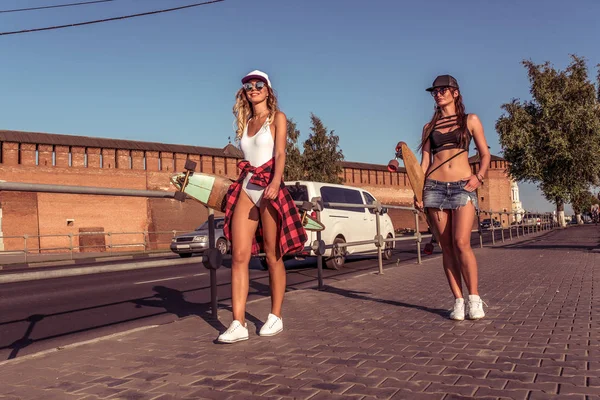 Zwei Freundinnen Sommerspaziergang Stadt Longboard Skateboard. Wochenendspaziergang, Sport-Fitness, Mädchen. Hintergrund Straßenbaum, Freizeitkleidung, freier Raum für Text. — Stockfoto