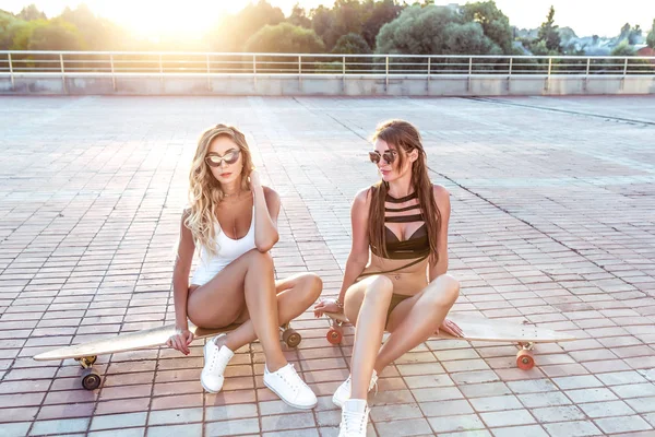 Zwei Mädchen schöne Freundinnen Sommer-Longboard-Skateboard. Ausruhen posieren für Wochenende gebräunte Figuren Fitness schlanke Mädchen. Mode-Hipster-Stil. lange Haare Sonnenbrille, Konzept Entspannungsspaß entspannend. — Stockfoto