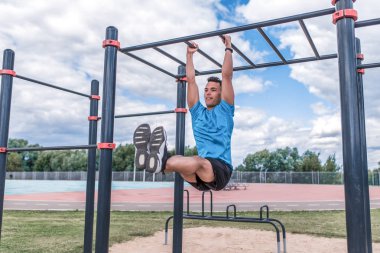Sporcu kendini yaz aylarında şehir sabah egzersizinde, basın egzersizinde, bacak bükerek, çim bulutu arka planında Crossbar 'a doğru çeker. Aktif gençlik yaşam tarzı, spor adamı.