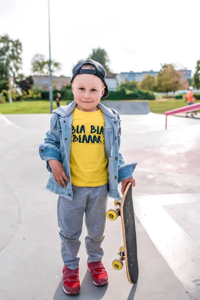 Little boy of 3-5 years old laughs, plays, relaxes, on summer autumn day in city park, fun casual clothes, skateboard board in his hand, casual clothes. — Stock fotografie