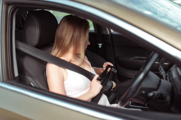 girl cars interior calls on phone, looks in rearview mirror, parks parking lot of shopping center, holds it fastened by steering wheel. Woman in summer sunglasses in city wearing a pink dress.