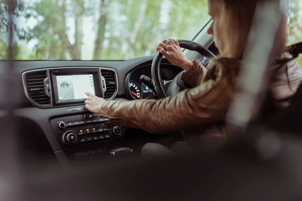 girl in car, selects application on touch screen display, navigation in car, a brown leather jacket, finding a route in summer and autumn in forest park. Right-hand drive, left-hand drive.