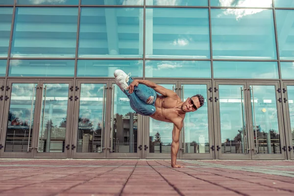 Erkek sporcu, erkek dansçı yaz şehri. Arka plandaki cam pencerelerde camlar var. Bronzlaşmış gövde, break dans tarzı hızlı, fitness sporu hip hop hareketli. Şehir kültürü, sokak dansı. Akrobatik egzersizler.