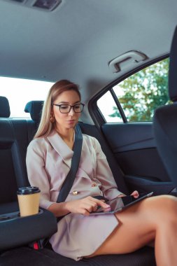 Kadın Tablet Yolu 'nda çalışıyor. Güzel, modern bir kız. Birinci sınıf araba koltuğuna bağlı. Vip taksi, pembe ceket, internet uygulaması, internet üzerinden çalışma.