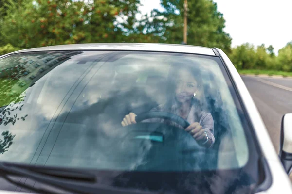 Женщина за рулем автомобиля, крупным планом лобовое стекло, задним отражением облака дороги деревьев, белый седан бизнес-класса, летом, осенью и весной, на дороге в движении . — стоковое фото