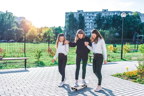 Adolescentes em camisolas, 3 alunas namoradas, verão no outono e primavera na cidade, skate feliz sorrindo se divertindo, fim de semana depois da escola . — Fotografia de Stock