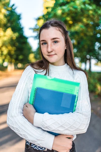 Bella ragazza adolescente 13-15 anni, si trova nel parco primaverile autunno estivo, tiene cartelle di libri di quaderni con libri di testo il suo concetto di mano che impara scuola college. Educazione i bambini studiano in città . — Foto Stock