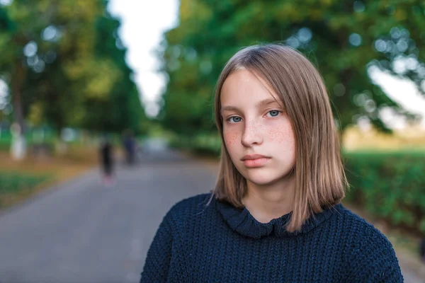 Portrait of teenager girl 12-15 years old, in summer in park, autumn day. Free space, resting after school lessons, on street. In sweater, close-up, freckles. Emotions of calm and do not care. — Stock Photo, Image