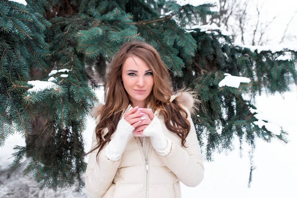Beautiful girl in warm white jacket, winter in snowy park, a background of Christmas tree and white snow, with mug of warm coffee tea. Happy smiling, resting winter resort weekend. — Stock Photo, Image