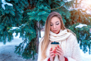 Güzel bir kız ceket aşağı atkı kış karlı parkı, arka plan ladin beyaz kar, sıcak bir fincan kahve çayı, ısınma, kış tatili hafta sonu dinlenme. Duygular zevk keyfi. Boş alan metni.